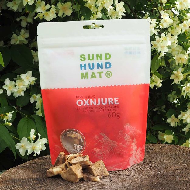Frystorkad oxnjure från Sund hundmat kommer i en praktisk återförslutningsbar påse. Oxnjuren är lite större och fyrkantiga i sin form. Påsen är korallfärgad och vit.