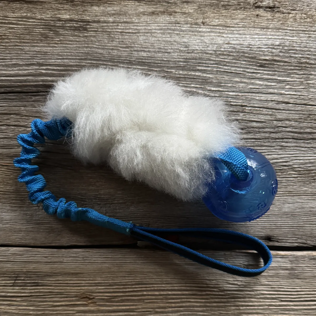 Hälge är en hundleksak med blå boll och blått expanderhandtag. Vitt svenskt fårskinn.