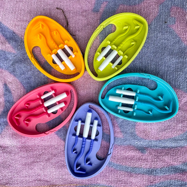 Fästingplockare med tre små kofötter i varje förpackning. Färgerna orange, grön, turkos, lila och rosa visas på bilden.